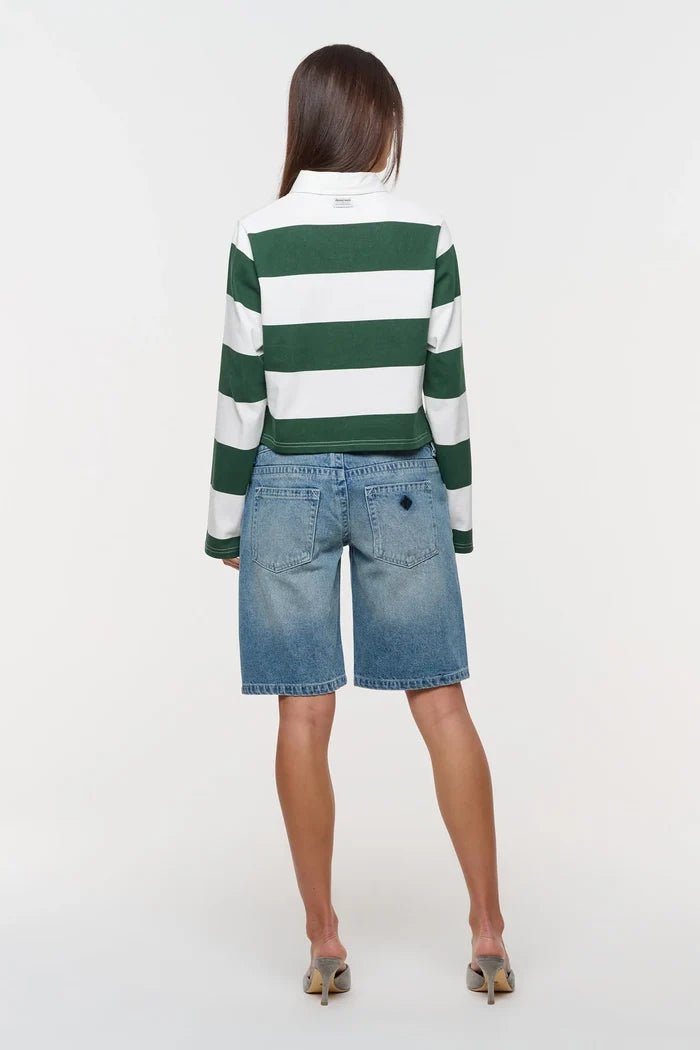 A woman shown from the back wearing a green and white horizontally striped long-sleeve top and light blue denim shorts, standing against a plain white studio background.
