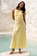 Woman in a yellow dress standing against a white marble wall.