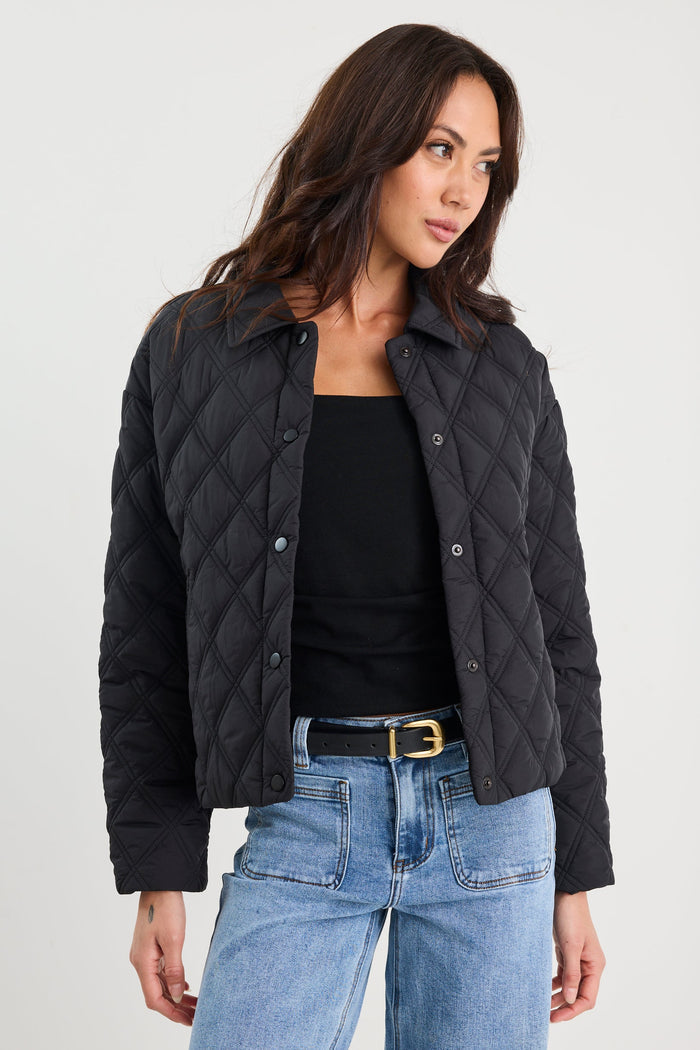 Woman wearing a black quilted jacket and blue jeans on a white background