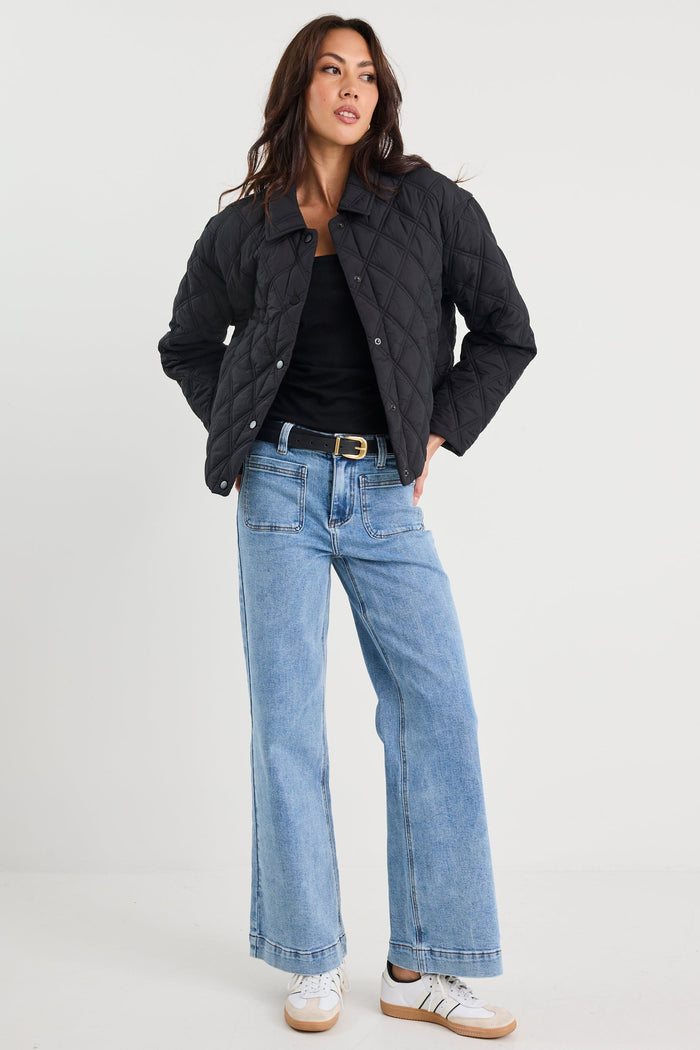 Woman wearing a black jacket, black top, blue jeans, and white sneakers on a white background