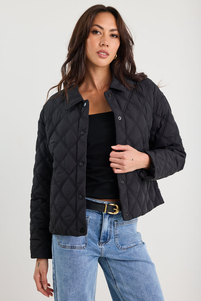 Woman wearing a black quilted jacket and blue jeans against a white background