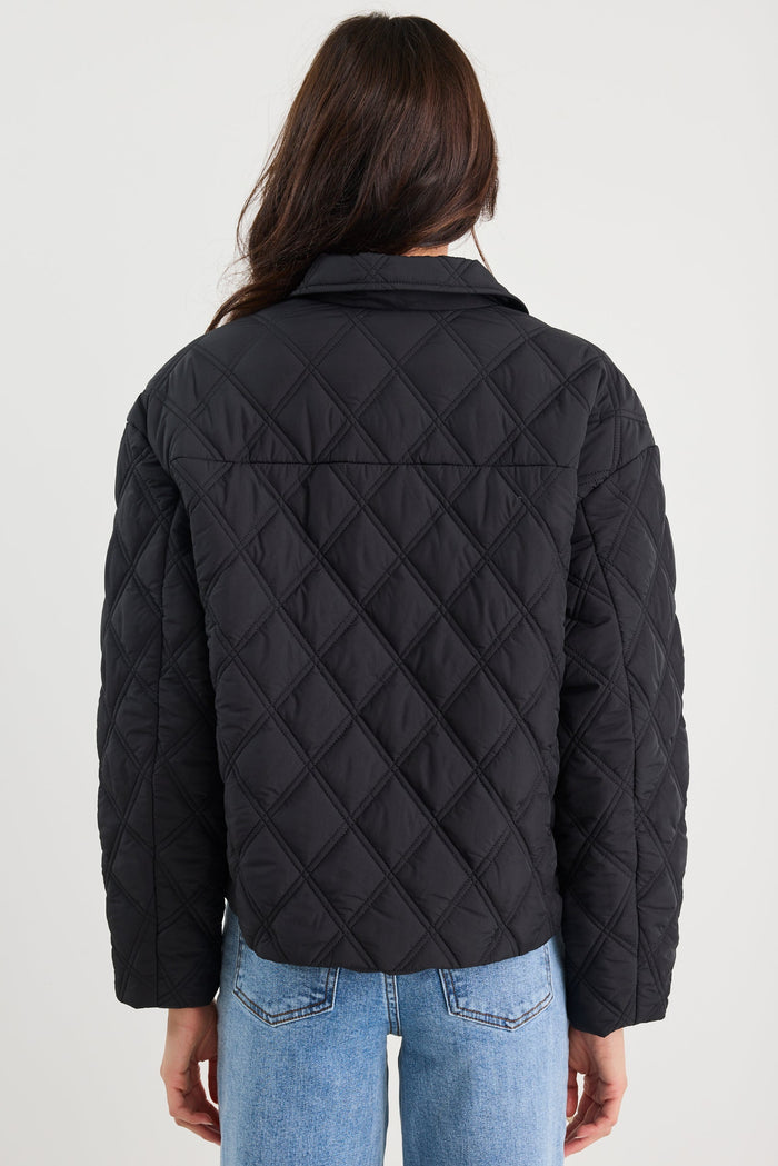 Person wearing a black quilted jacket and blue jeans on a white background