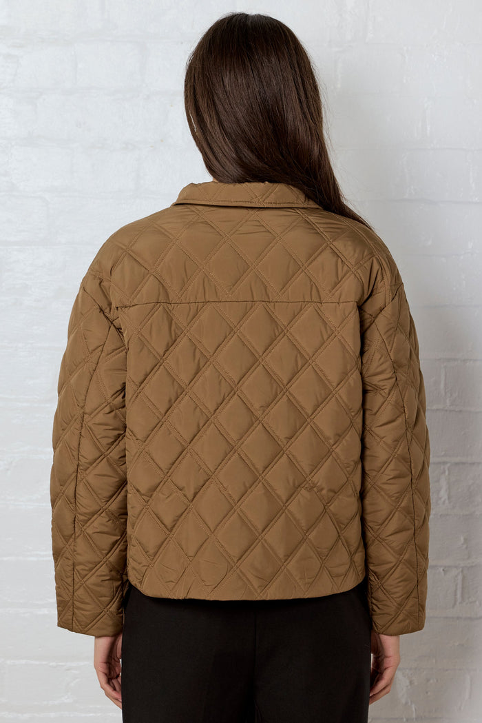 Person wearing a quilted brown jacket against a white brick wall
