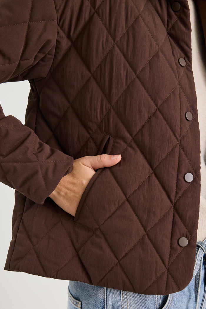Brown quilted jacket with diamond pattern worn by a person, focusing on the jacket's texture and design.
