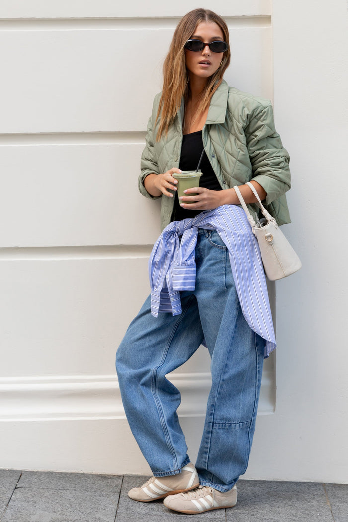Woman in stylish outfit leaning against a white wall