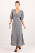 A woman modeling a long gray midi dress with puff sleeves, a V-neckline, and a tie detail at the bust, photographed against a plain light studio background.