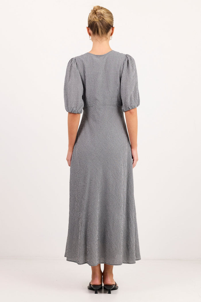 A woman viewed from the back wearing a gray midi dress with short puff sleeves and black flat shoes, standing against a plain white studio background.