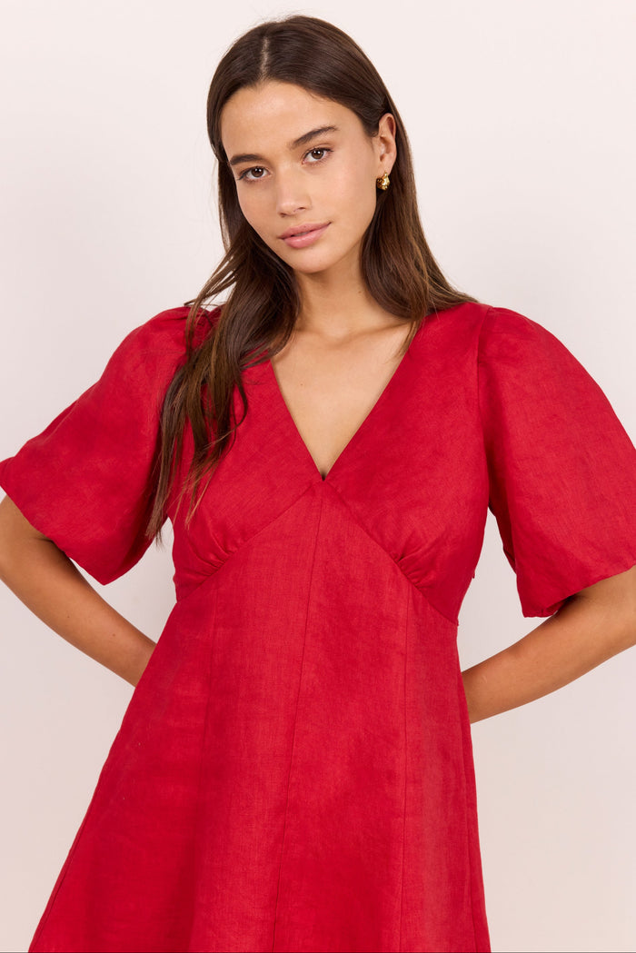 A woman modeling a vibrant red dress with short puff sleeves, a deep V-neckline, and a gathered waist, set against a plain light background.