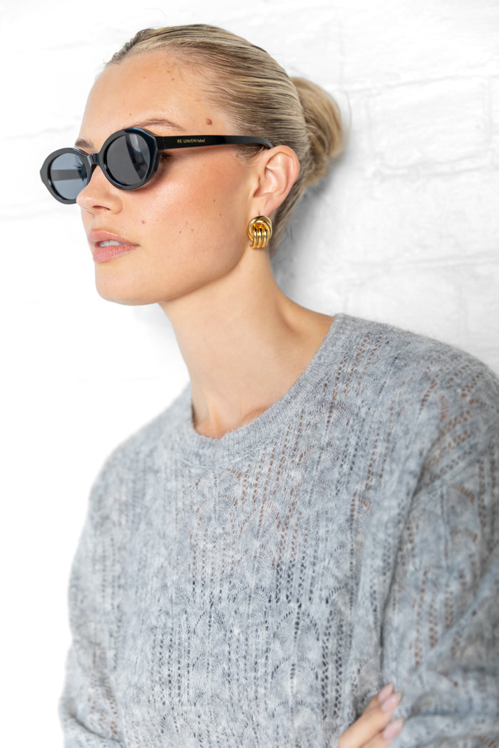 Woman wearing sunglasses and a gray sweater against a white background