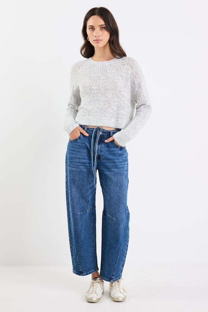 Woman wearing a light gray sweater and blue jeans on a white background