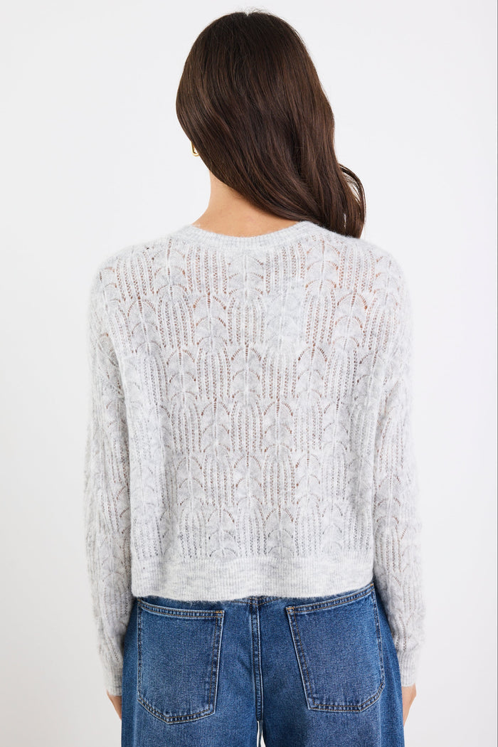Person wearing a light gray cable knit sweater and blue jeans on a white background