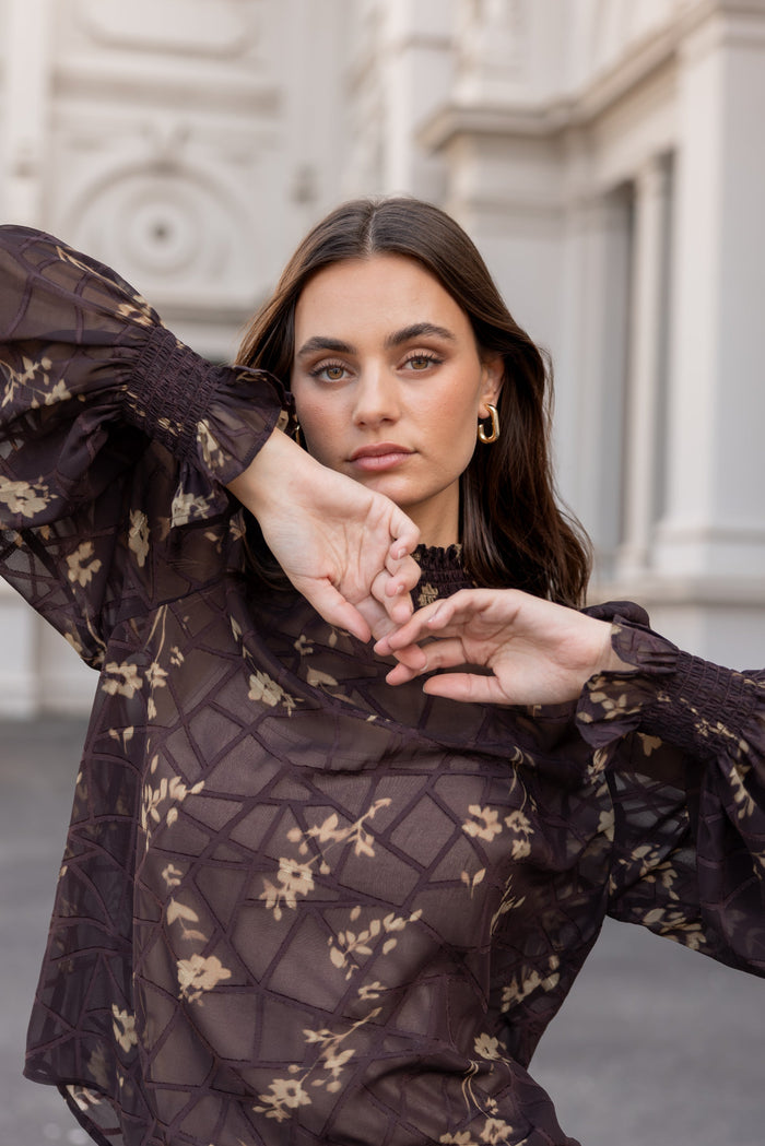 Woman wearing a dark floral lace dress with a blurred architectural background