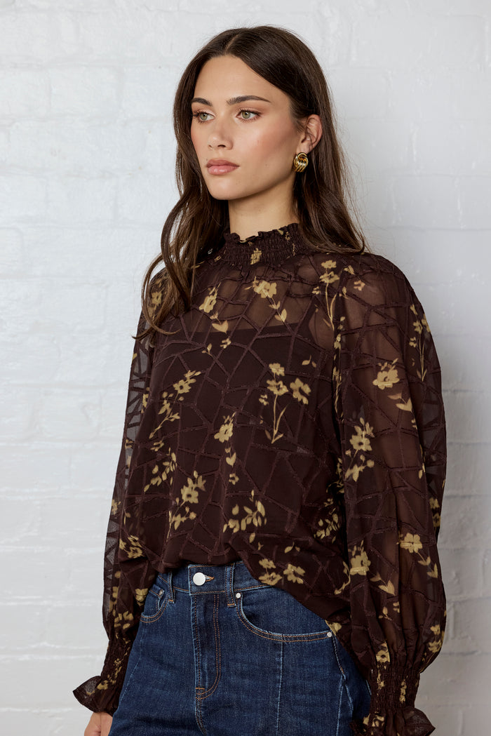 Woman wearing a dark floral blouse against a white brick wall