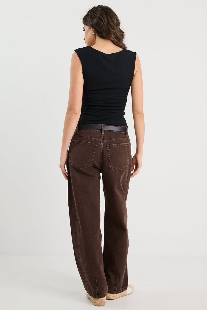 Woman wearing a black sleeveless top and brown wide-leg jeans on a white background