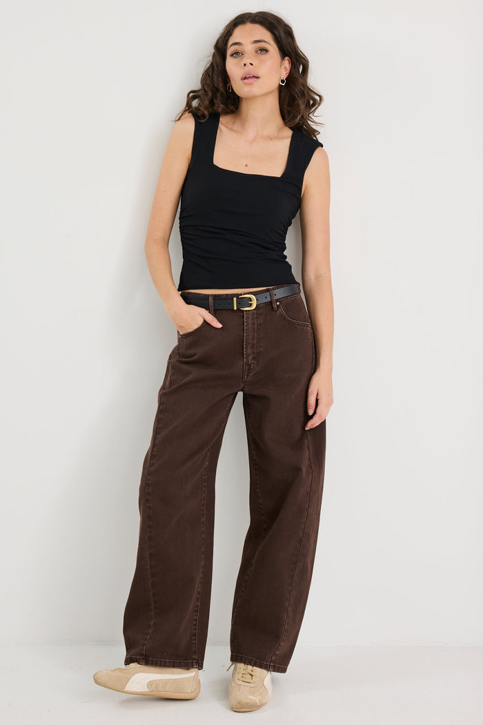 Woman wearing a black tank top and brown pants on a white background