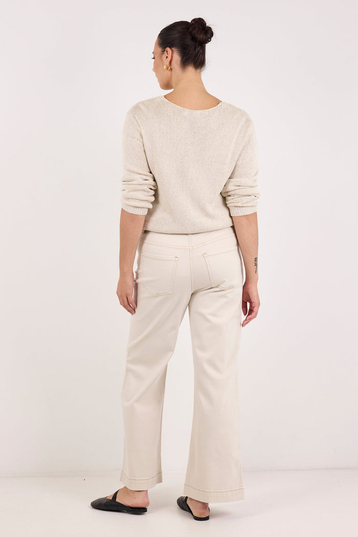 A woman is shown from the back wearing a light beige knit long-sleeve top and matching wide-leg trousers, paired with black flat shoes, against a plain white studio background.