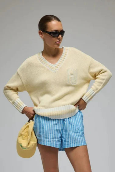 Person wearing a light yellow sweater, blue checkered shorts, and white sneakers on a gray background