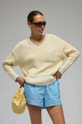 Person wearing a light yellow sweater, blue checkered shorts, and white sneakers on a gray background