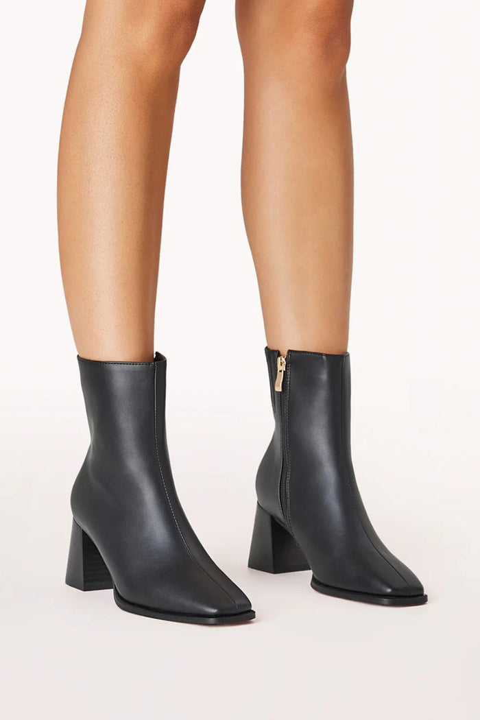 Black ankle boots with block heels worn by a person on a white background
