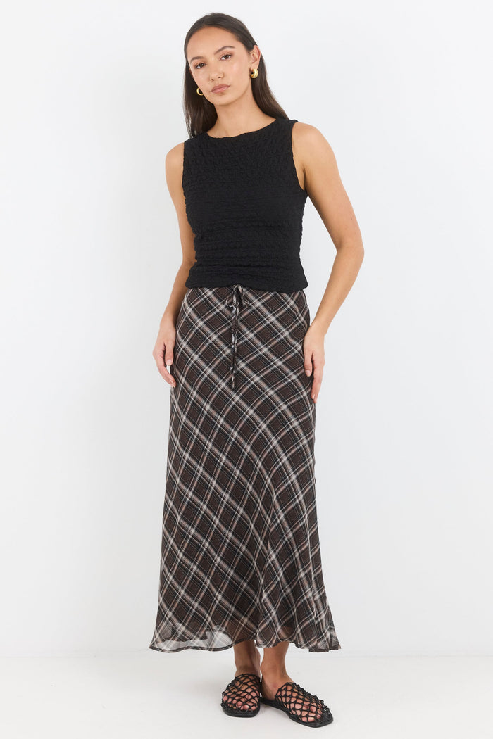 Woman wearing a black sleeveless top and plaid skirt on a white background