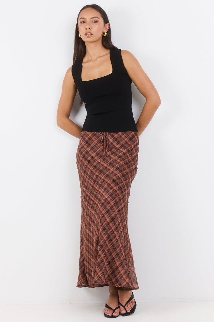 Woman wearing a black top and patterned skirt on a white background