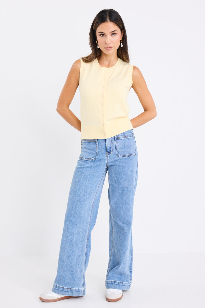 Woman wearing a sleeveless yellow vest with button-down front and crew neck, paired with blue jeans.