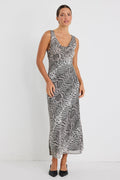 Woman wearing a sleeveless, bias-cut midi dress with a charcoal snake print, styled with black heels against a white wall.