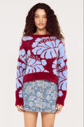 Woman wearing a red and blue floral-patterned sweater with a denim skirt on a white background