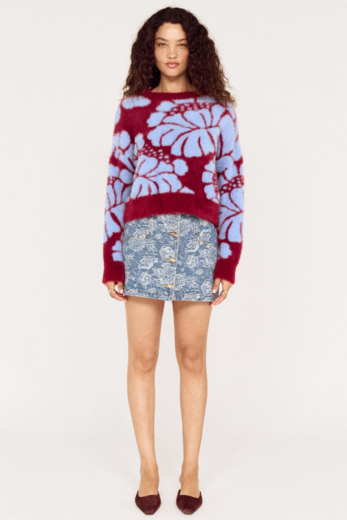 Woman wearing a red and blue floral sweater with a denim skirt on a white background