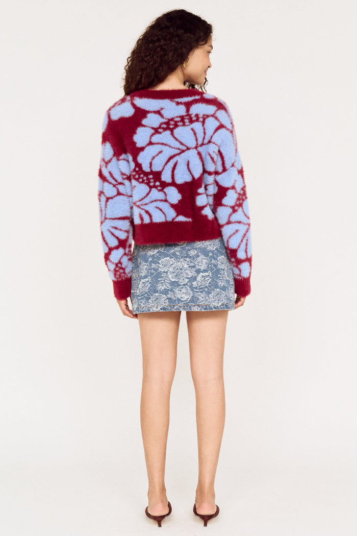 Person wearing a patterned sweater and denim skirt on a white background