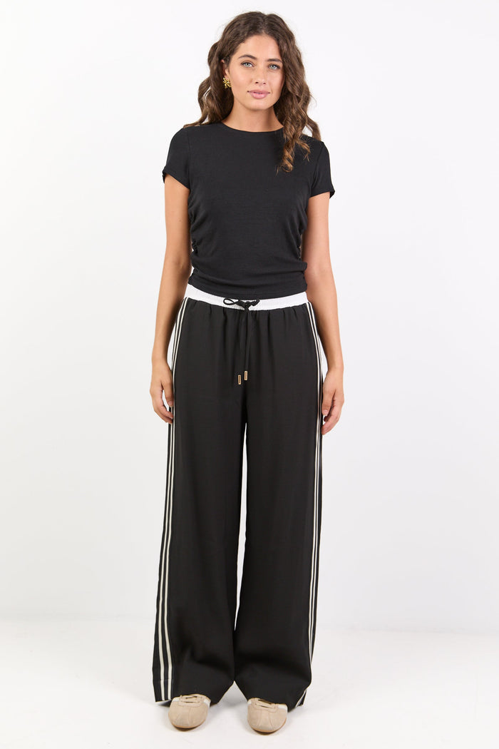 Woman wearing a black t-shirt and black pants with white stripes on a white background