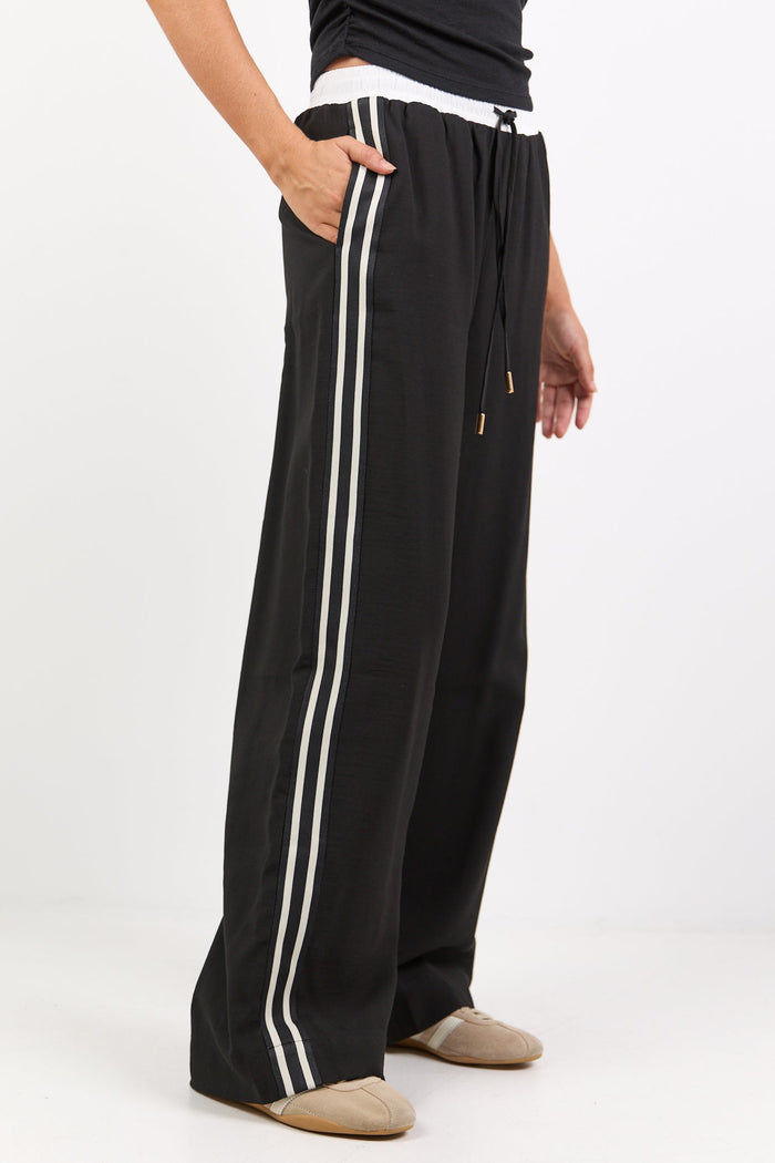 Person wearing black wide-leg pants with white stripes on a white background