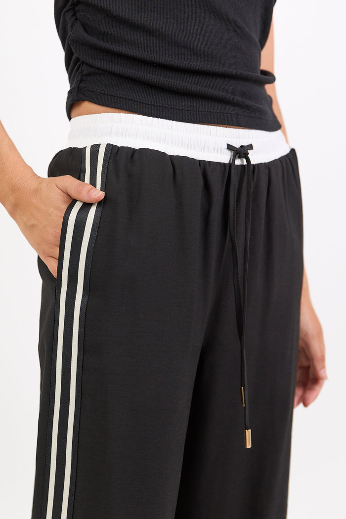 Person wearing a black top and black pants with white stripes on a white background