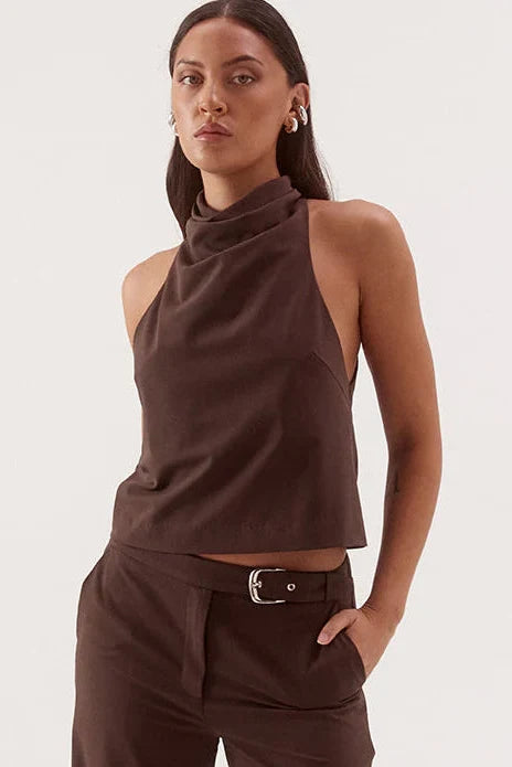 A woman modeling a dark brown sleeveless halter crop top and matching wide-leg trousers with a belt, against a plain light gray studio background.