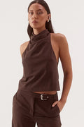 A woman modeling a dark brown sleeveless halter crop top and matching wide-leg trousers with a belt, against a plain light gray studio background.