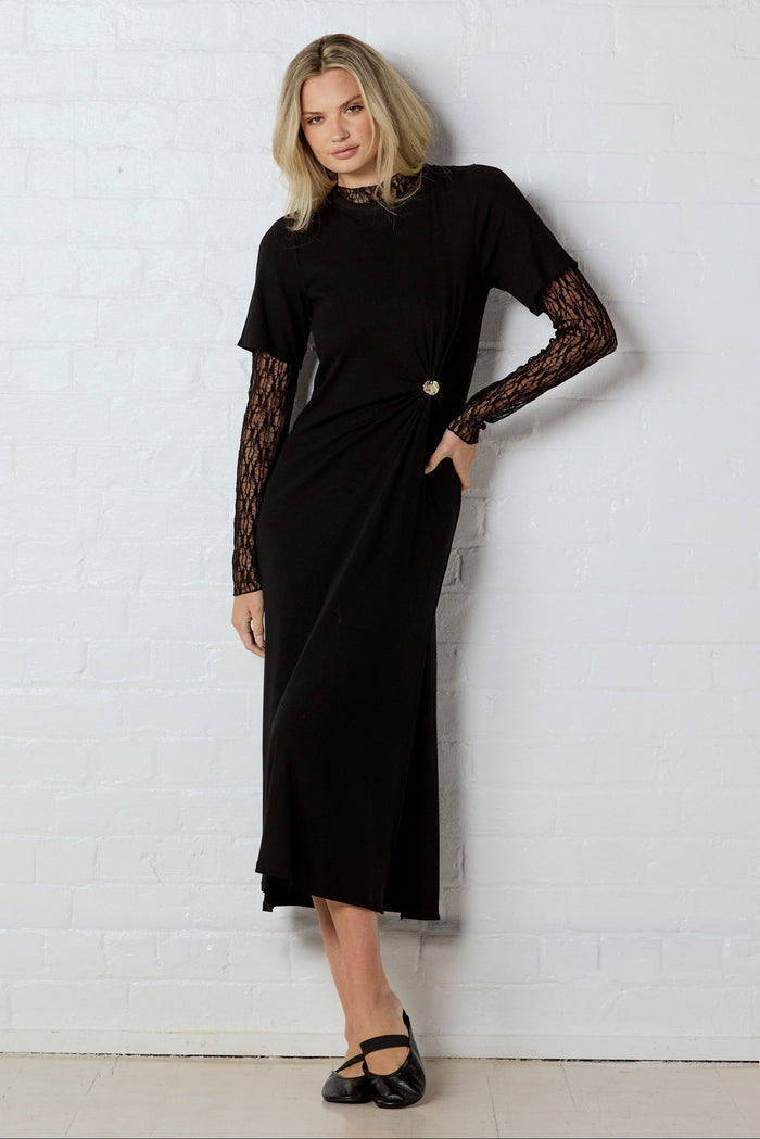 Woman wearing a black dress with lace sleeves against a white wall