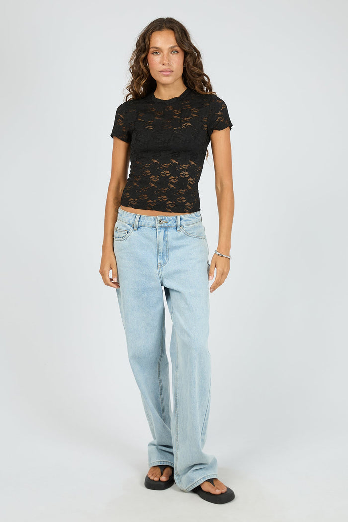 Woman wearing a black lace top and light blue jeans on a white background