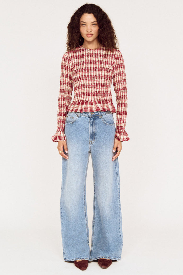 Woman wearing a red and white checkered top and blue jeans on a white background