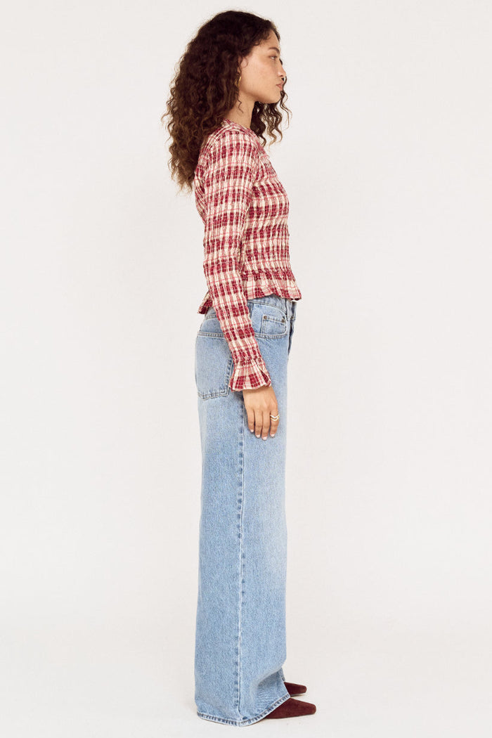Person wearing a red and white checkered shirt and light blue jeans on a white background