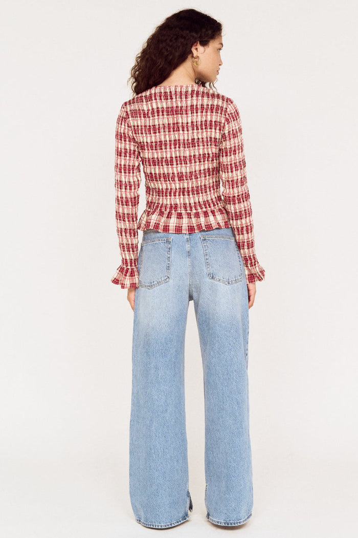 Woman wearing a red and white checkered shirt and light blue jeans on a white background