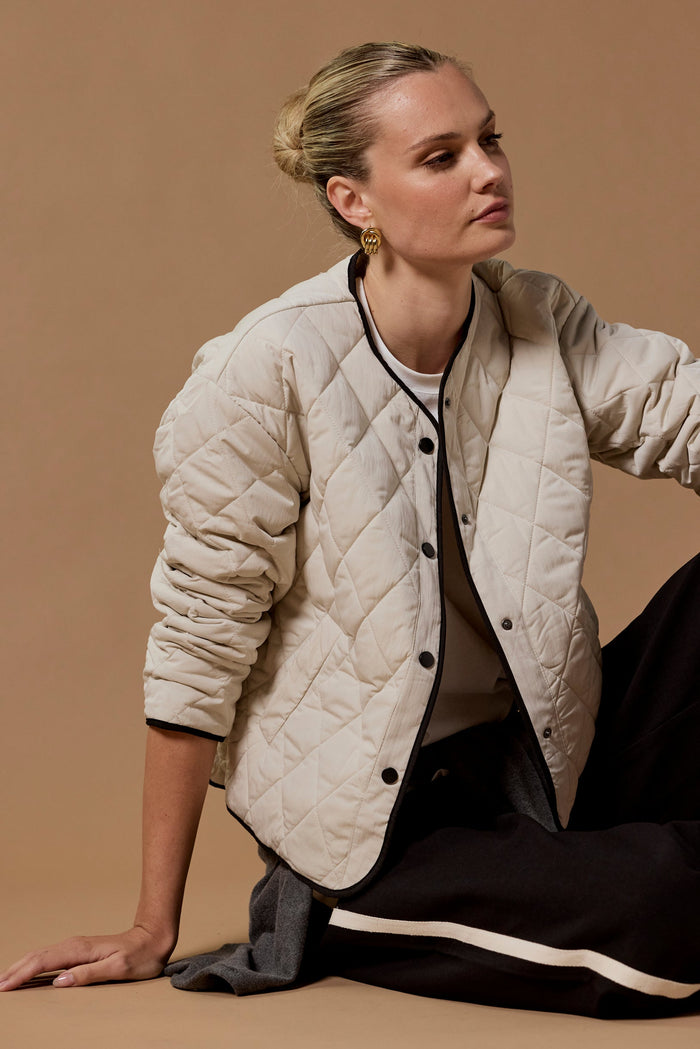 Woman wearing a beige quilted jacket sitting on a brown background