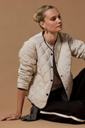 Woman wearing a beige quilted jacket sitting on a brown background