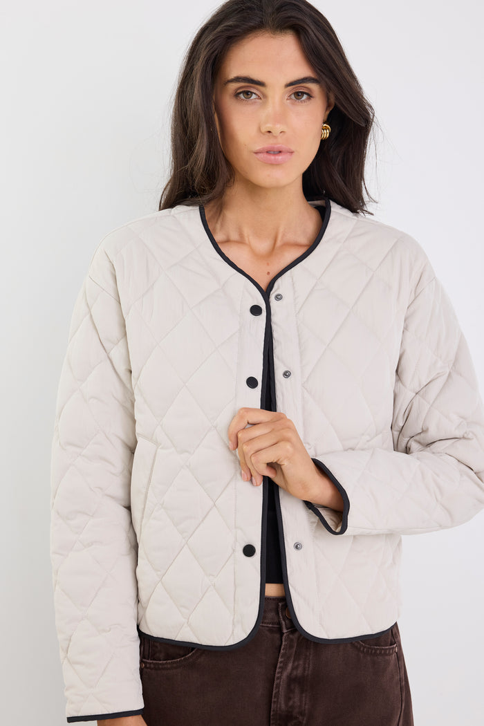 Woman wearing a beige quilted jacket with black trim on a white background