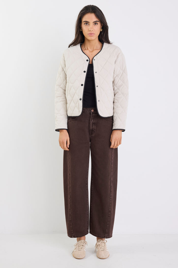 Woman wearing a beige quilted jacket, black top, and brown wide-leg jeans on a white background