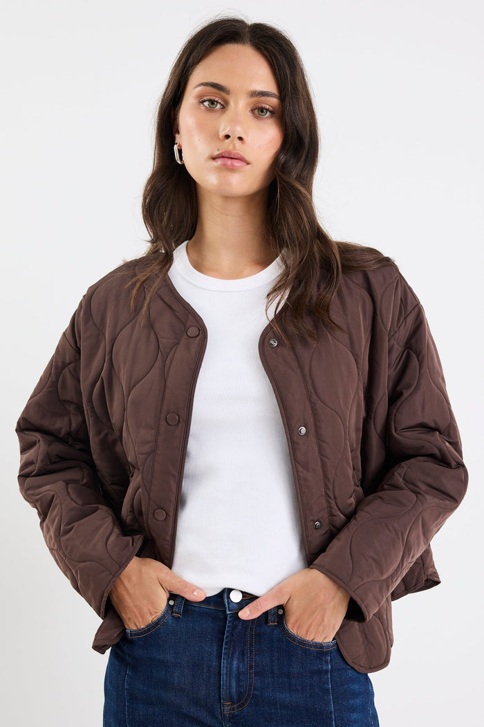 Woman wearing a brown jacket, white shirt, and blue jeans on a white background