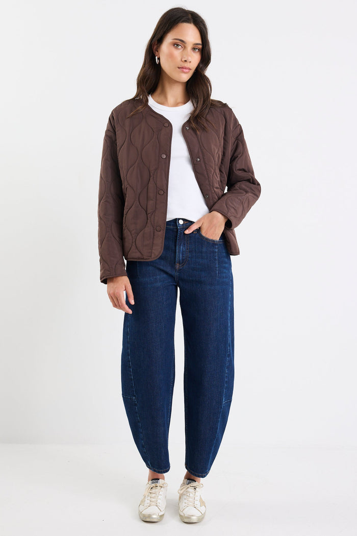 Woman wearing a brown jacket, white shirt, and blue jeans on a white background