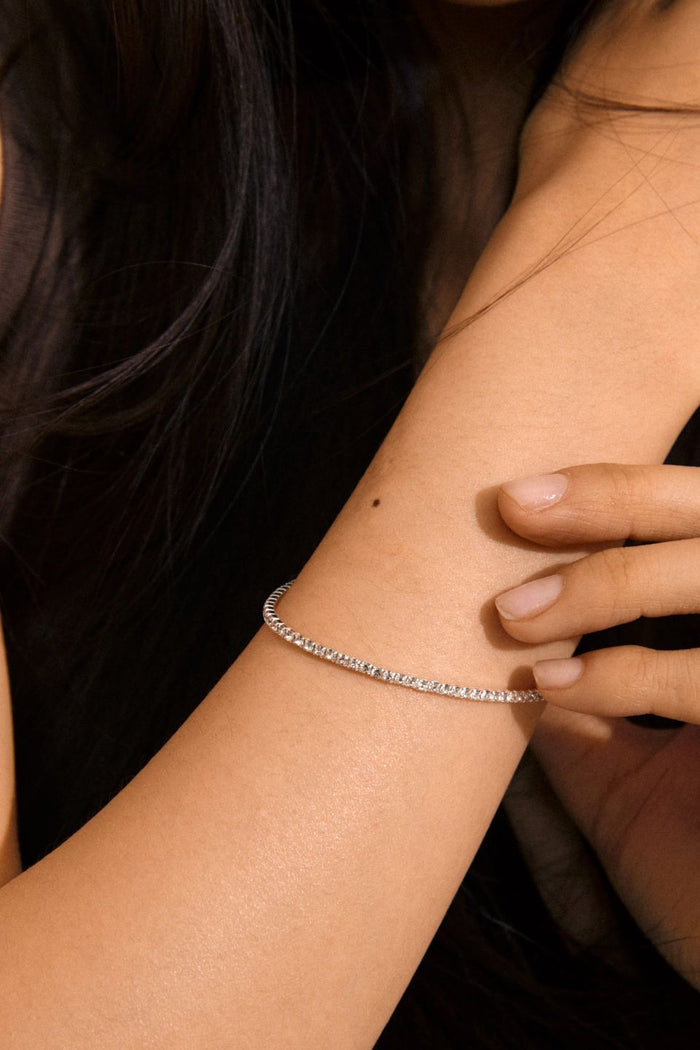 Close-up of a person's arm wearing a silver bracelet with a dark background