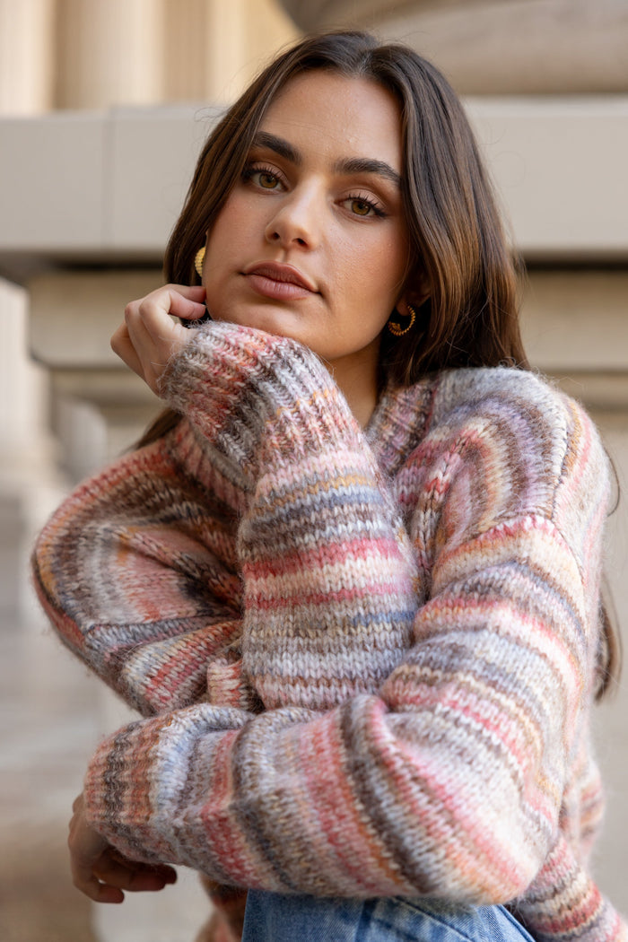Woman wearing a colorful striped sweater and blue jeans standing against a neutral background