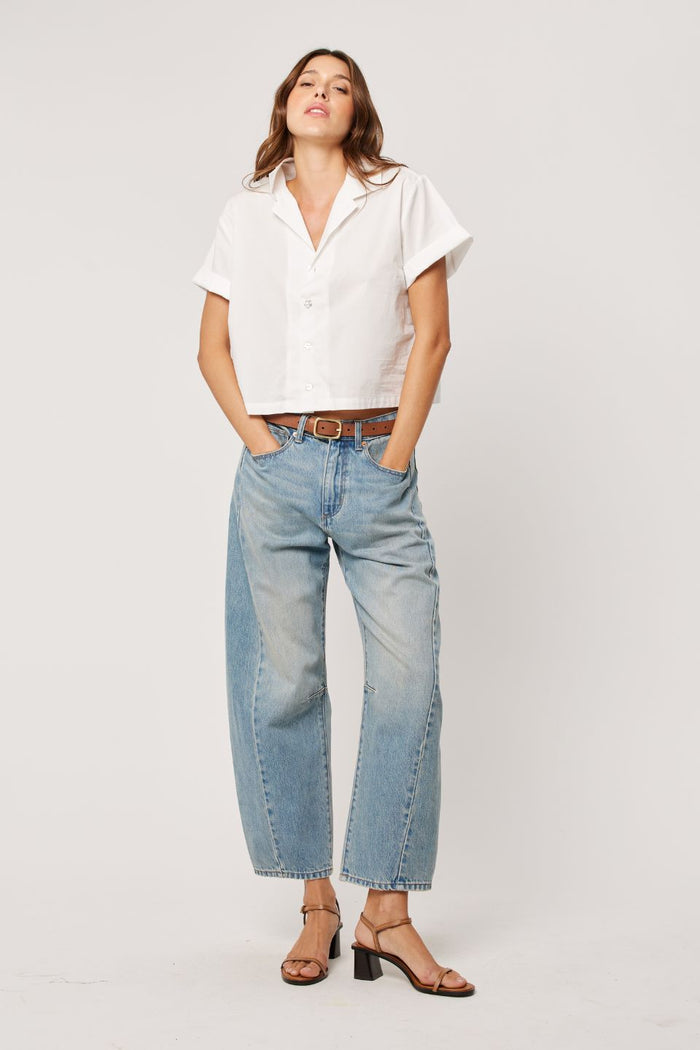 Woman wearing a white top with light wash blue barrel jeans