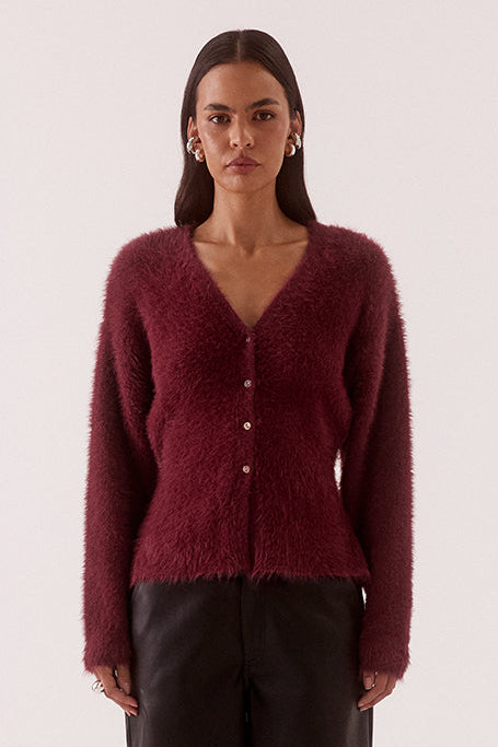 Woman wearing a burgundy cardigan and dark pants on a white background